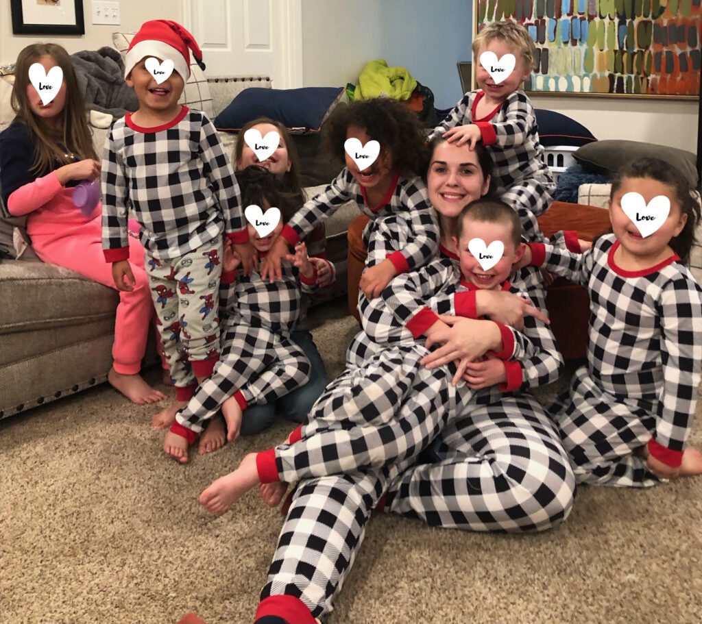 Foster mom posing with eight children in checkered Christmas pajamas.
