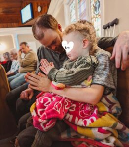A child sits next to her foster dad with her hands folded in prayer.