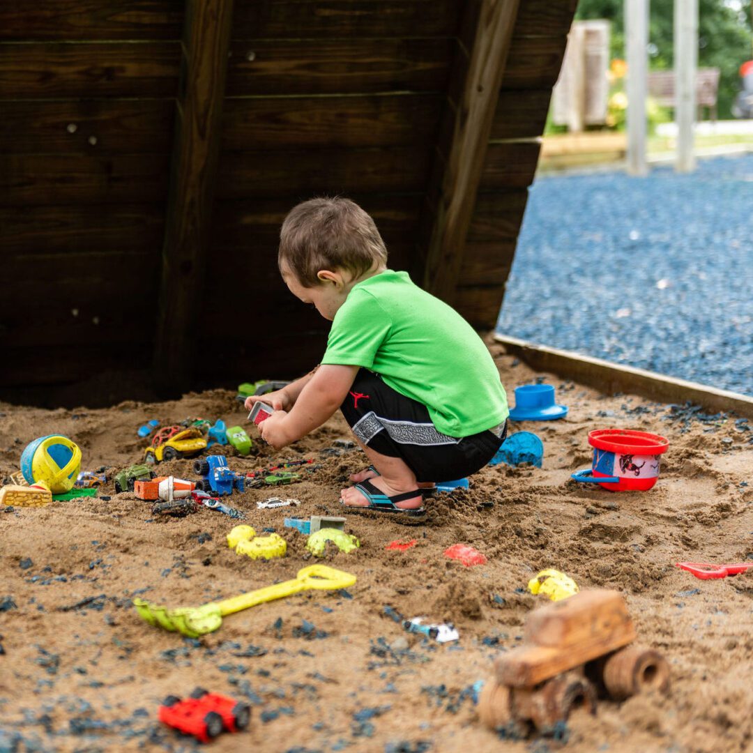 a child at The Hill plays in a sandbox, surrounded by colorful toys